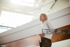 Young confident and happy businesswoman walking through office building. She is wearing business casual clothes and she is holding laptop in her hand